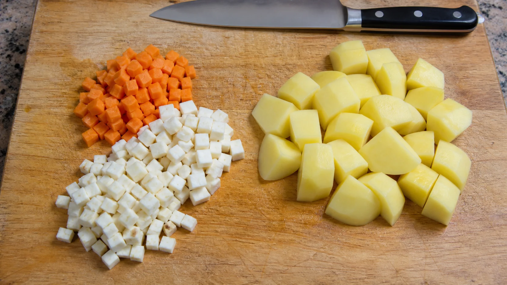Stejnoměrně nakrájená kořenová zelenina a větší kostky brambor na prkénku
