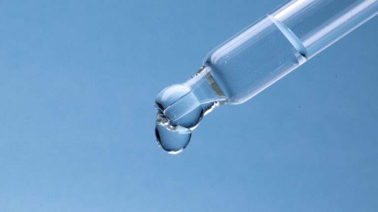 Žena si v koupelně nanáší pipetou sérum na hřbet ruky
